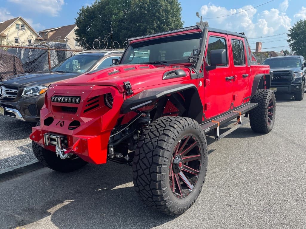 A red jeep with large tires parked in the street.